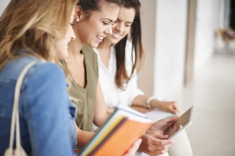 Trio de amigas sorrindo olhando para tablet; Veja quais cursos não precisam de estágio obrigatório para se formar